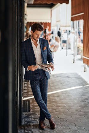 Handsome man in checked suit reading newspaper on the streetの写真素材