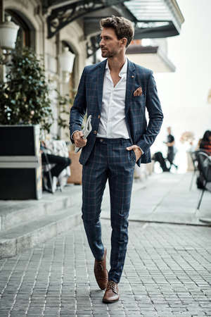 Handsome male model in checked suit walking on the street with newspaperの写真素材