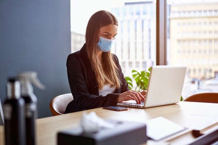 Businesswoman working on laptop wearing face masks protect from coronavirus in officeの写真素材