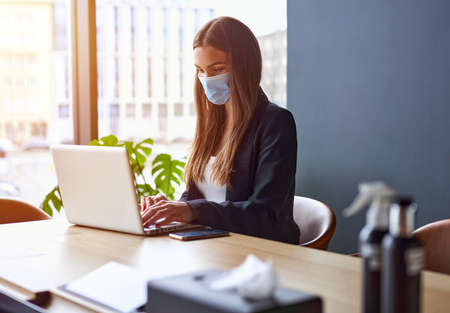 Businesswoman working on laptop wearing face masks protect from coronavirus in officeの写真素材