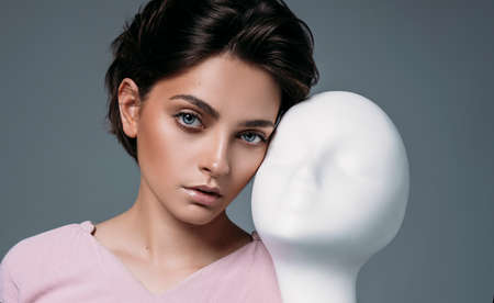 Portrait of young brunette woman with mannequin face isolated on gray backgroundの写真素材