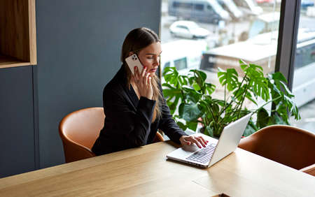 Business woman in home office working on laptop and talking on the phoneの写真素材