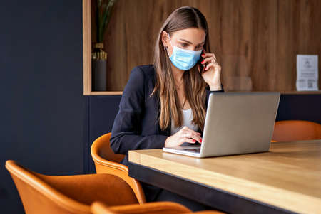 Business woman talking on the phone and working on laptop wearing face masks protect from coronavirus in officeの写真素材