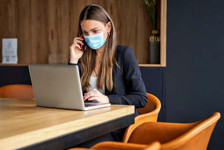 Business woman talking on the phone and working on laptop wearing face masks protect from coronavirus in officeの写真素材