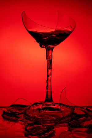 Broken glass with wine stands on a glass mirror table on a red backgroundの写真素材