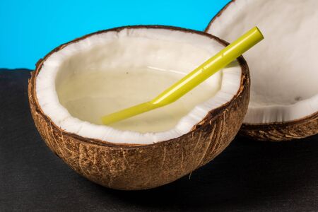 two half of coconut with a plastic cocktail straw lies on a stone tray on a blue background close-upの写真素材