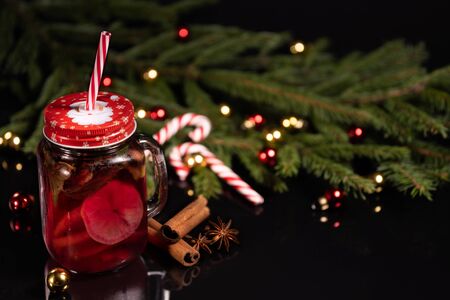 Christmas cocktail with lemon and spices cinnamon and star anise on a black background of a Christmas tree with toys and candy canの写真素材