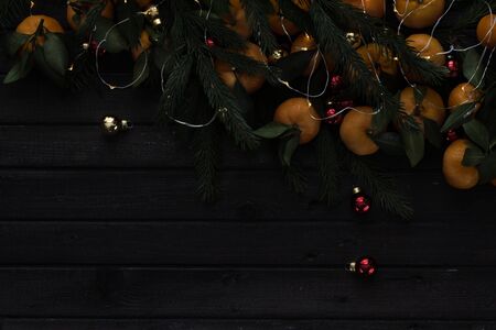 Christmas tangerines with leaves lie in the branches of spruce, garlands and Christmas toys on a wooden table. Top view. Night photo.の写真素材