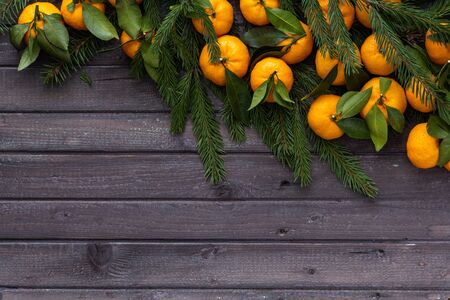 Christmas tangerines with leaves lie in the branches of spruce on a wooden tableの写真素材