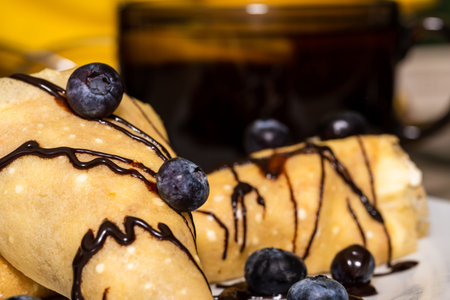 three pancakes on a white plate twisted with cream inside, watered with chocolate and blueberries...