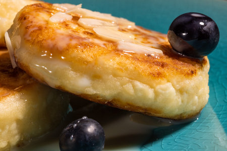 cheese pancake with almonds and blueberries poured with condensed milk on a blue plate, closeup