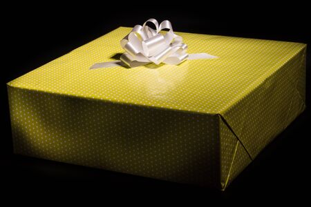 Large gift box wrapped in yellow speckled paper and a white bow on a black background, closeupの写真素材