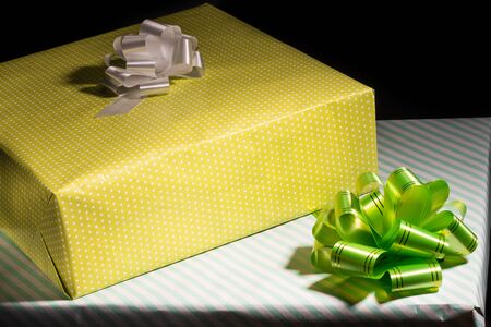 Two large gift boxes wrapped in yellow and white speckled paper and a white and green bow on a black background, closeupの写真素材