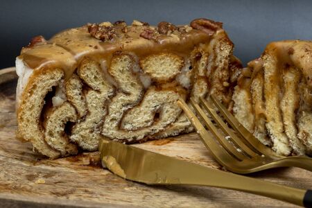 Side view of a cut cinnamon roll poured with caramel and nuts on a wooden tray with a fork and knife on a black background, side viewの写真素材