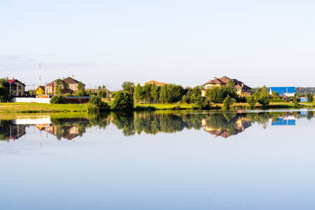 country houses on the lake behind the trees, the reflection of houses in the water, a windless dayの写真素材