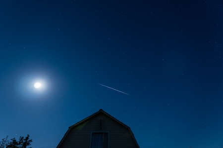 Cloudless, blue, summer night. Starlink's sputnic fly over the house against the moon. Deep night, starry sky.の写真素材