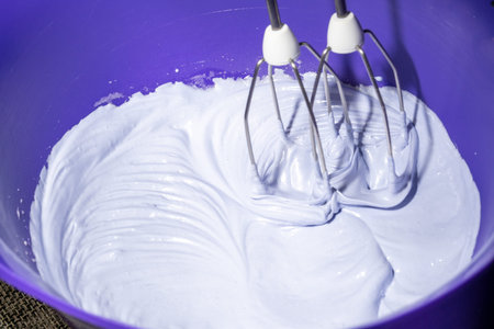 Cooking, whipping the lilac meringue with a mixer, in a purple bowl, close-up.