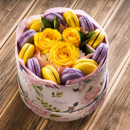 macaroons, purple and yellow, in a box with yellow roses, on a wooden table, close-up.の写真素材