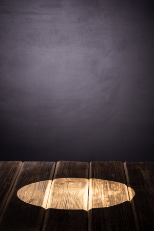 A ray of light on a wooden table against the background of a black wall for chalk, spruce branchesの写真素材
