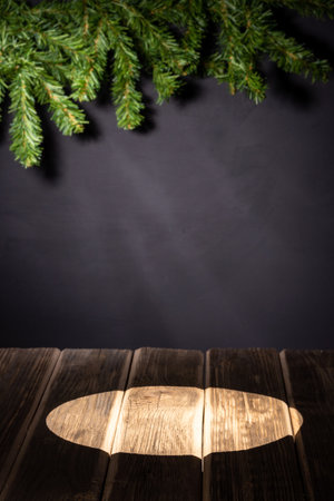A ray of light on a wooden table against the background of a black wall for chalk, spruce branchesの写真素材