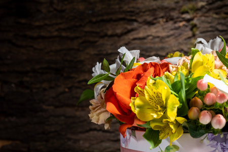 basket of fresh flowers consisting of Rose Carnation Iris Alstroemeria Hypericum and pistachio, close-up, against the background of the bark of a tree.の写真素材