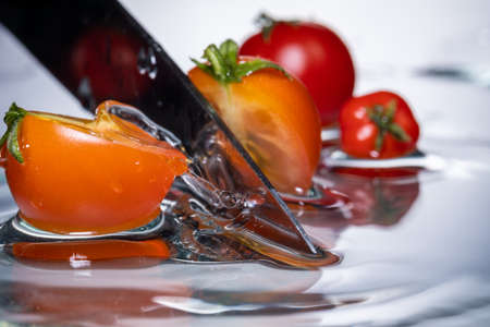 small red cherry tomatoes cut with a knife, in water with falling drops, frozen motion, close-upの写真素材