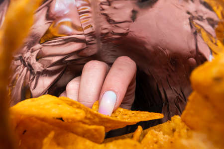 a woman's hand reaches into the package with nacho chips, the view from the bag, close-up.の写真素材