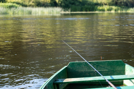 An old wooden, green boat on the river. Fishing rod with a float in the river. Fishingの写真素材