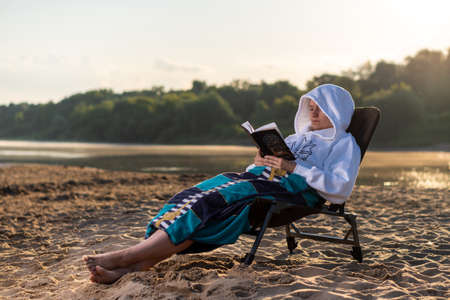 A girl on the bank of the river in a yellow swimsuit and shertas, reads. Breakfast by the river. Fruits.の写真素材