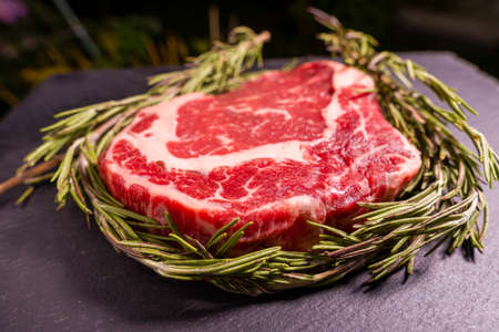 Raw marbled beef steak on a stone tray with rosemary.の写真素材