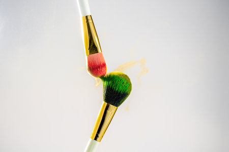 Two white with gold makeup brushes on a white background. Powder brush, fine powder particles around.の写真素材