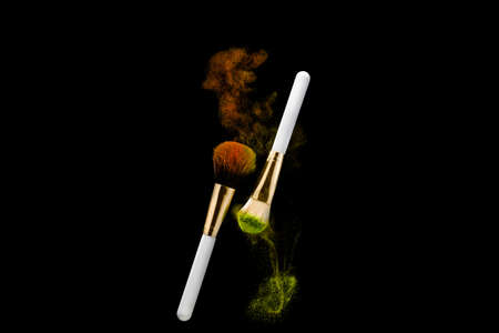 Two white with gold makeup brushes on a black background. Powder brush, fine powder particles around.の写真素材