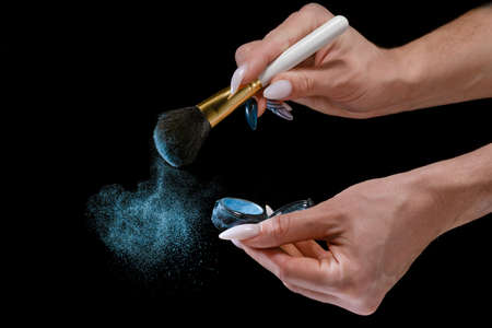 A girl with a long manicure applies blue powder to a brush. Small particles of powder are all around.の写真素材