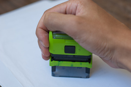 Hand holding a rubber stamp on white paper.の写真素材