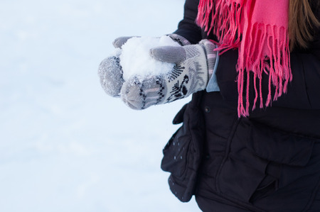 A teenage girl is holding in her hands, dressed in woolen mittens, snow in the winter.の写真素材