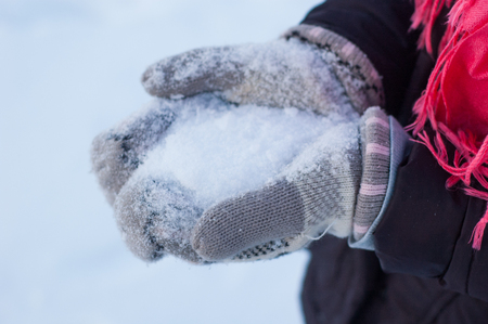 A teenage girl is holding in her hands, dressed in woolen mittens, snow in the winter.の写真素材