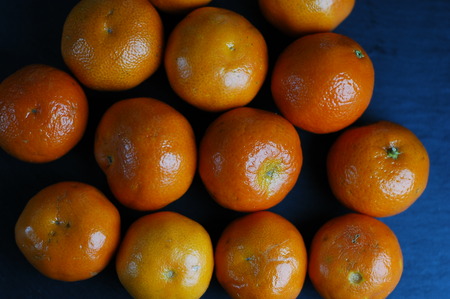 Unpeeled mandarins on a dark background with hard light.の写真素材