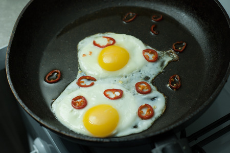 Two fried eggs with chili pepper in a skillet.の写真素材
