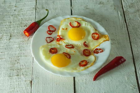 Two fried eggs with chili pepper on white table.の写真素材