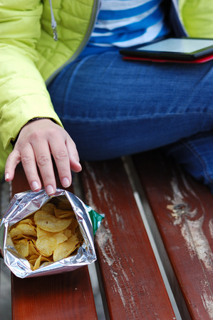 The girl is reading an e-book and eating chips.の写真素材
