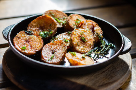 Fried potatoes with rosemary in a small cast-iron pan on the table.