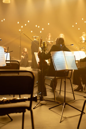 Violinist reading sheet music in a studio with empty chairs and blurred choir in the backgroundの写真素材