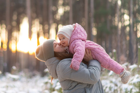 Mother lifting her little daughter in a pink jumpsuit in a snowy forestの写真素材