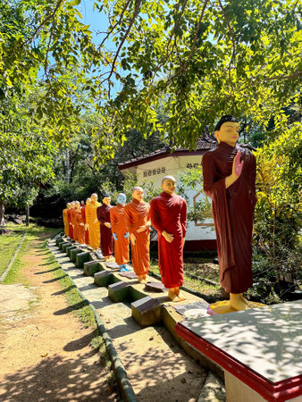 Colorful statues of Buddhist monks walking in line under leafy trees at a temple.の写真素材
