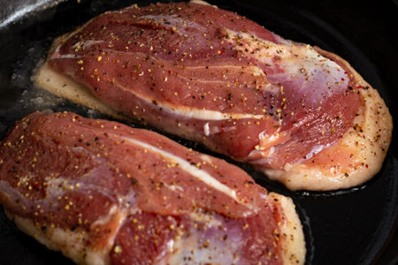 two duck breasts are fried in a pan, seasoned with salt and a mixture of peppersの写真素材
