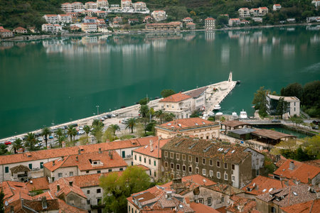 Aerial view of Kotor old town with red tiled rooftops and pier extending into turquoise bay,...