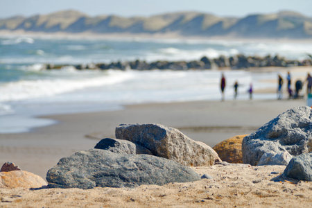 Foreground with rocks. Blurred and unidentified people walking on the beach on the North sea coast in Denmark.の写真素材
