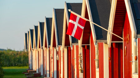 Row of wooden beach huts with a Danish flag in the foreground at the baltic sea coastの写真素材