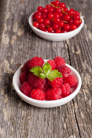 Fresh red currant and sweet raspberries on wooden table, verticalの写真素材