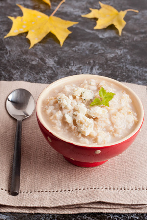 Oatmeal porridge with cheese in bowl and autumn leaves on black table, rustic breakfast, vertical, close up, top viewの写真素材